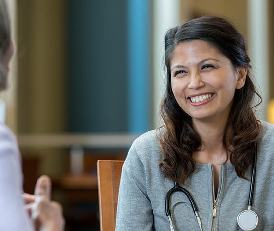 Caring mid adult female doctor talks with an unrecognizable senior female patient.