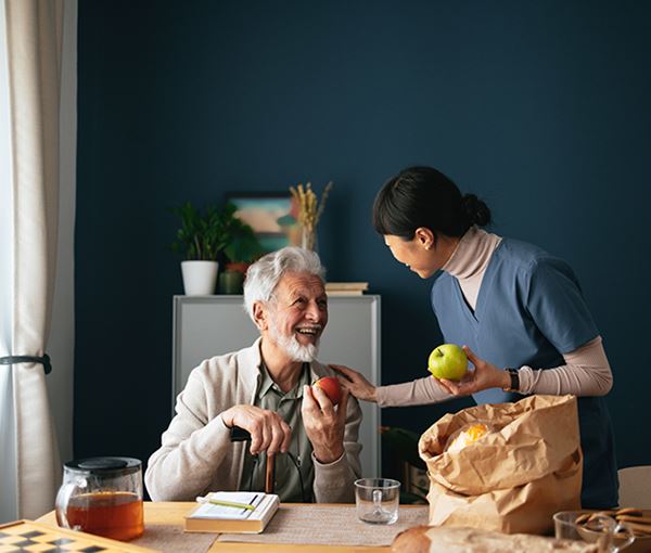 Happy Nurse Delivering Groceries To Senior Man At His Home